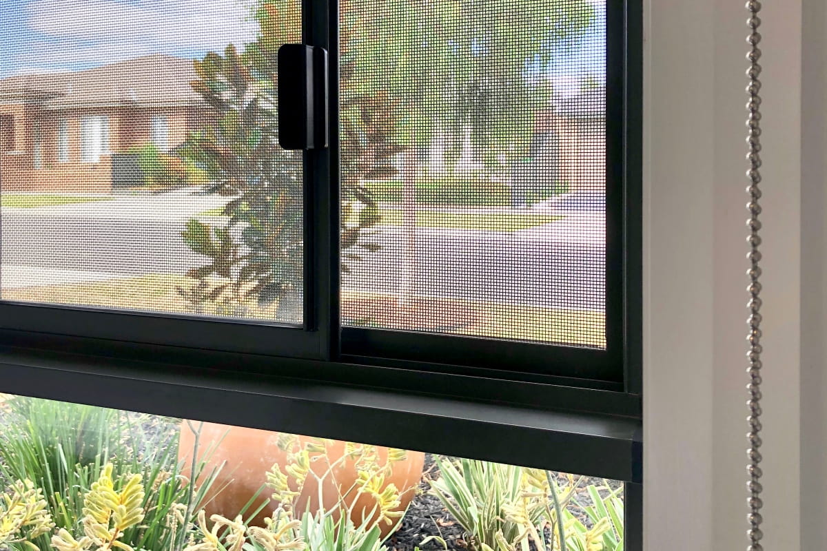 What Is a Bushfire Attack Level (BAL) and Why It Matters for Your Home 1 Black-framed security window screen overlooking a landscaped garden, illustrating the importance of suitable window screens for bushfire attack level requirements.