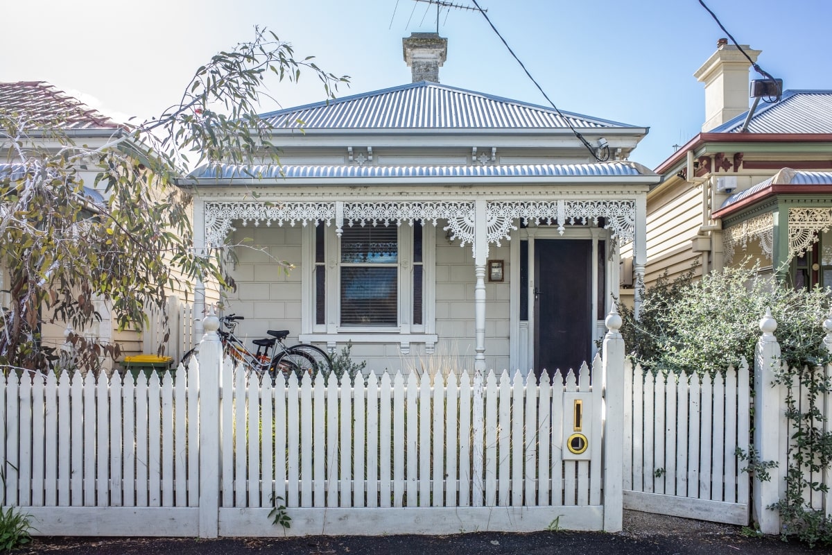 A white, Victorian era home with intricate lacework and white picket fence.