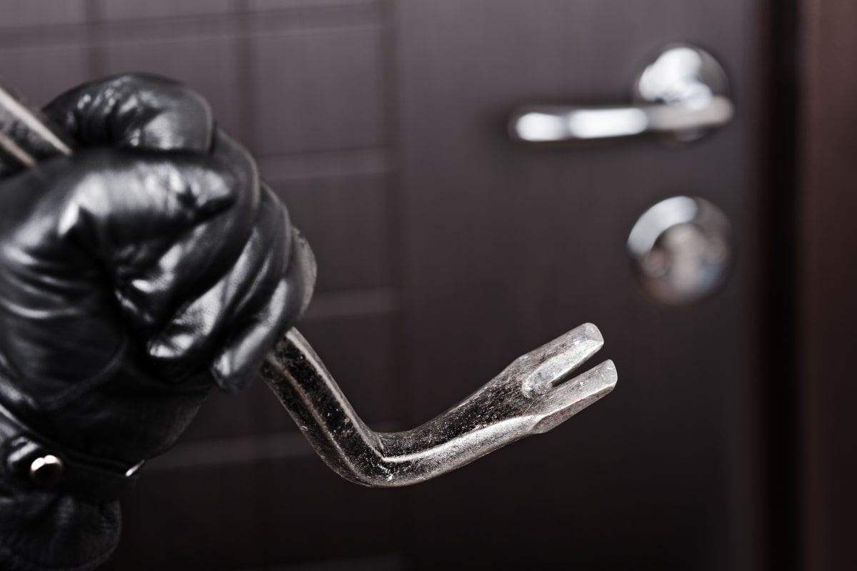Image of a would-be burglar with a crowbar at a residential door, highlighting deadlocks as a deterrent for such crimes.