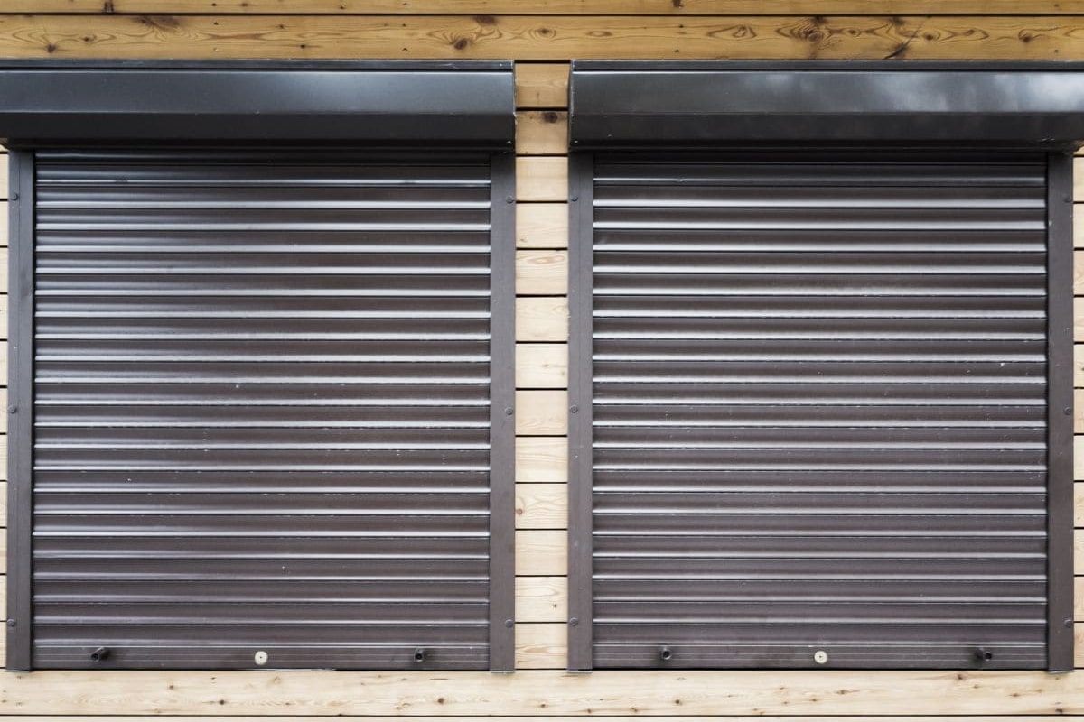 Two closed brown roller shutters on a timber-clad building.