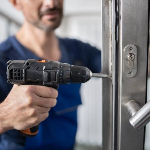 Locksmith fixing locks on security door with drill.