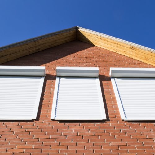 Three white roller shutters installed on windows of brick home.