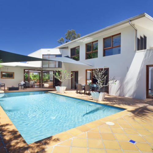 Modern home with large windows overlooking a pool, highlighting the need for fall prevention screens to improve window safety.