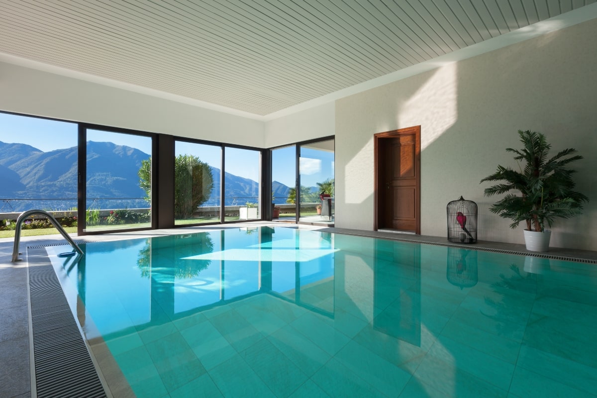 A indoor pool enclosed with large windows looking out at mountains.