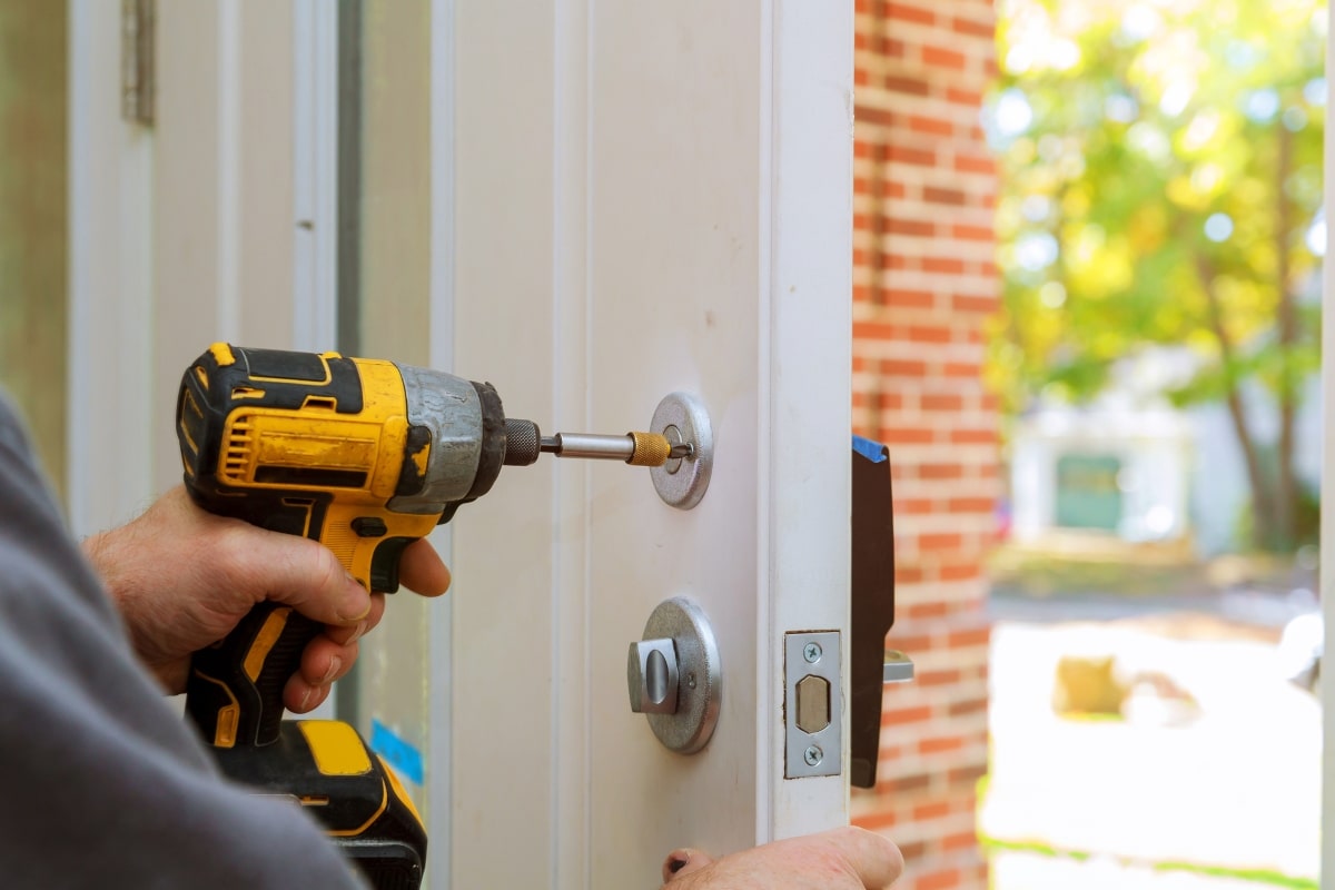 Hands of a man expertly fitting a dead lock into a door frame, indicating the importance of professional installation and maintenance of deadlocks.