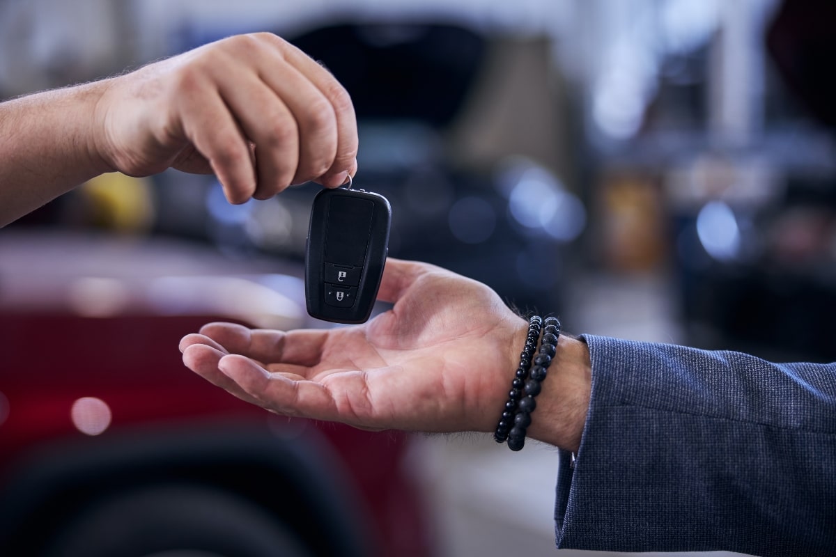 A hand holding a car key fob with a small, square transponder embedded in it, passing it over to another hand.