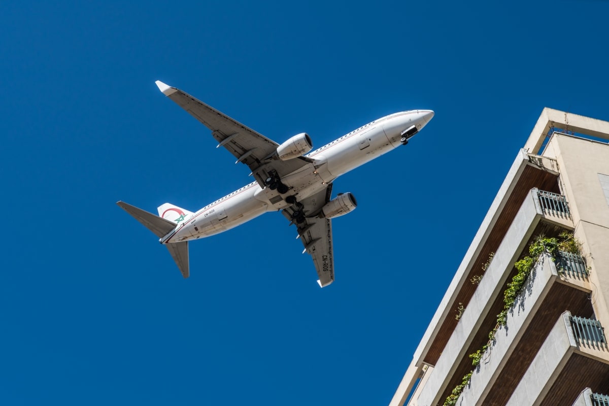 An aeroplane flying closely over a building, demonstrating the challenge of noise pollution in urban living and the potential noise-blocking solution of roller shutters.