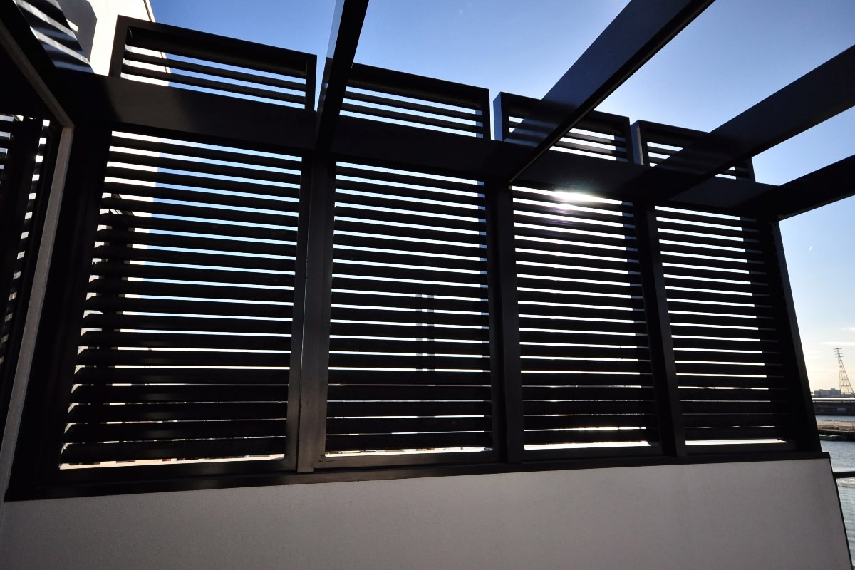Close-up view of a contemporary patio screen with linear slats, allowing controlled sunlight against a clear blue sky backdrop.