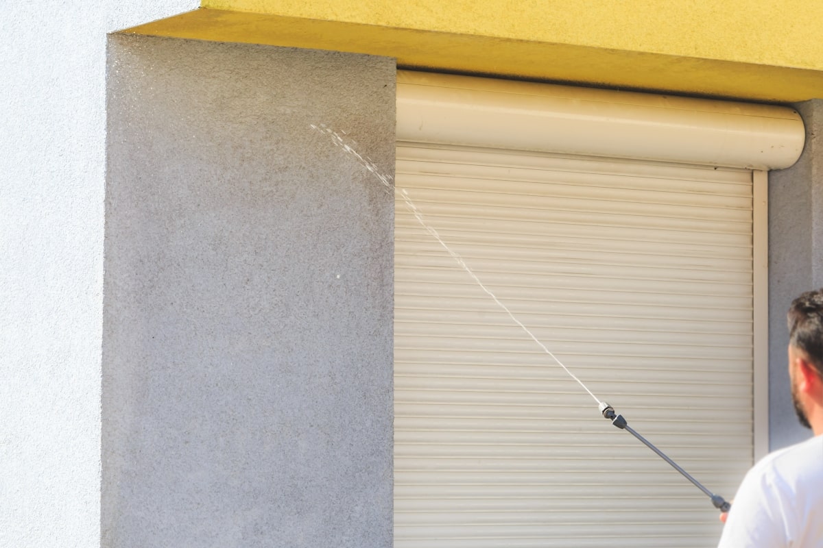 Man using hose to clean the outside of roller shutters.