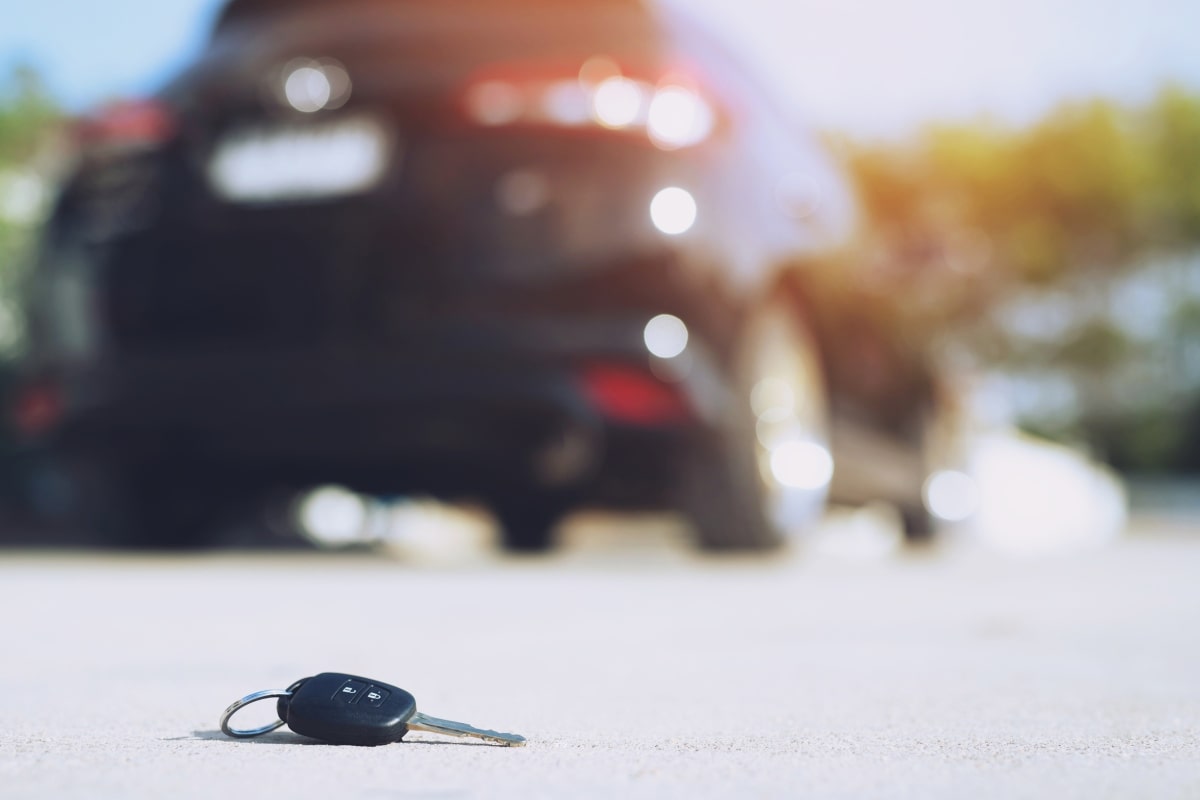 Low angle image of a transponder car key lying on the road with a blurry car in the background, illustrateing the concept of lost keys and the need for transponder key replacement.