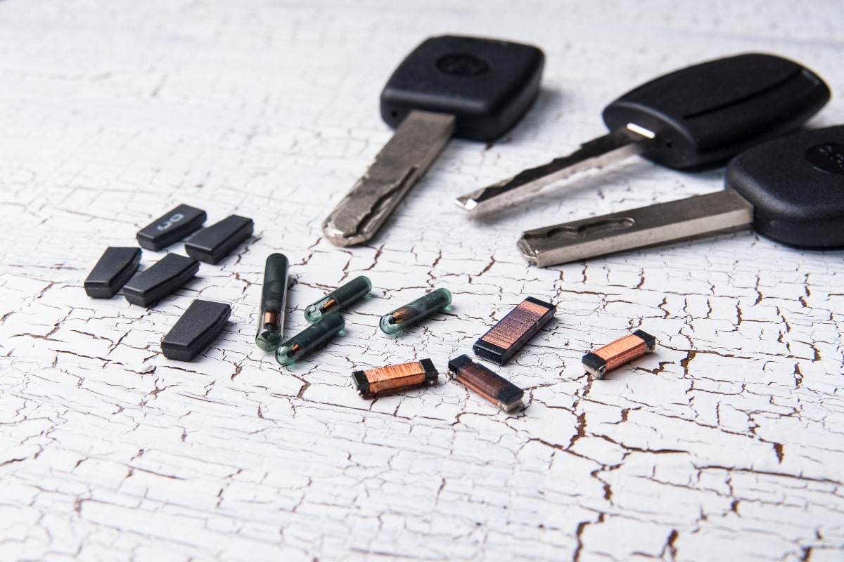 Image of three transponder car keys and RFID chips on a cracked white surface – an essential tool for car owner security! 