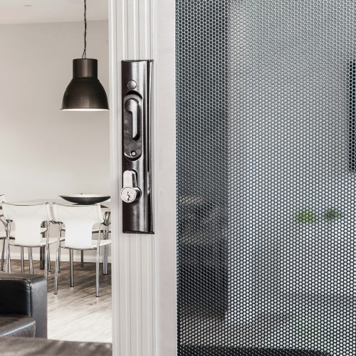 Sliding security door with black handle and triple lock feature, looking into a dining area.