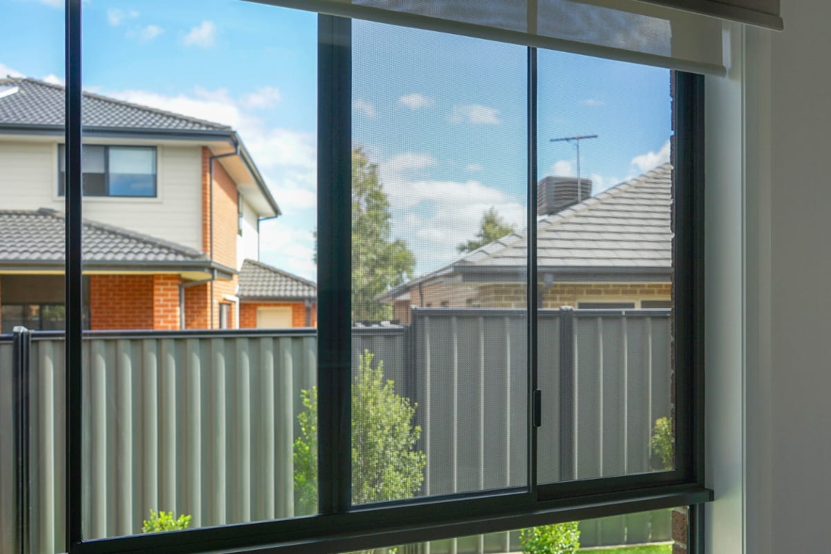 What Is a Bushfire Attack Level (BAL) and Why It Matters for Your Home 4 Sliding window featuring a black security screen and aluminium frame, with suburban houses visible outside.